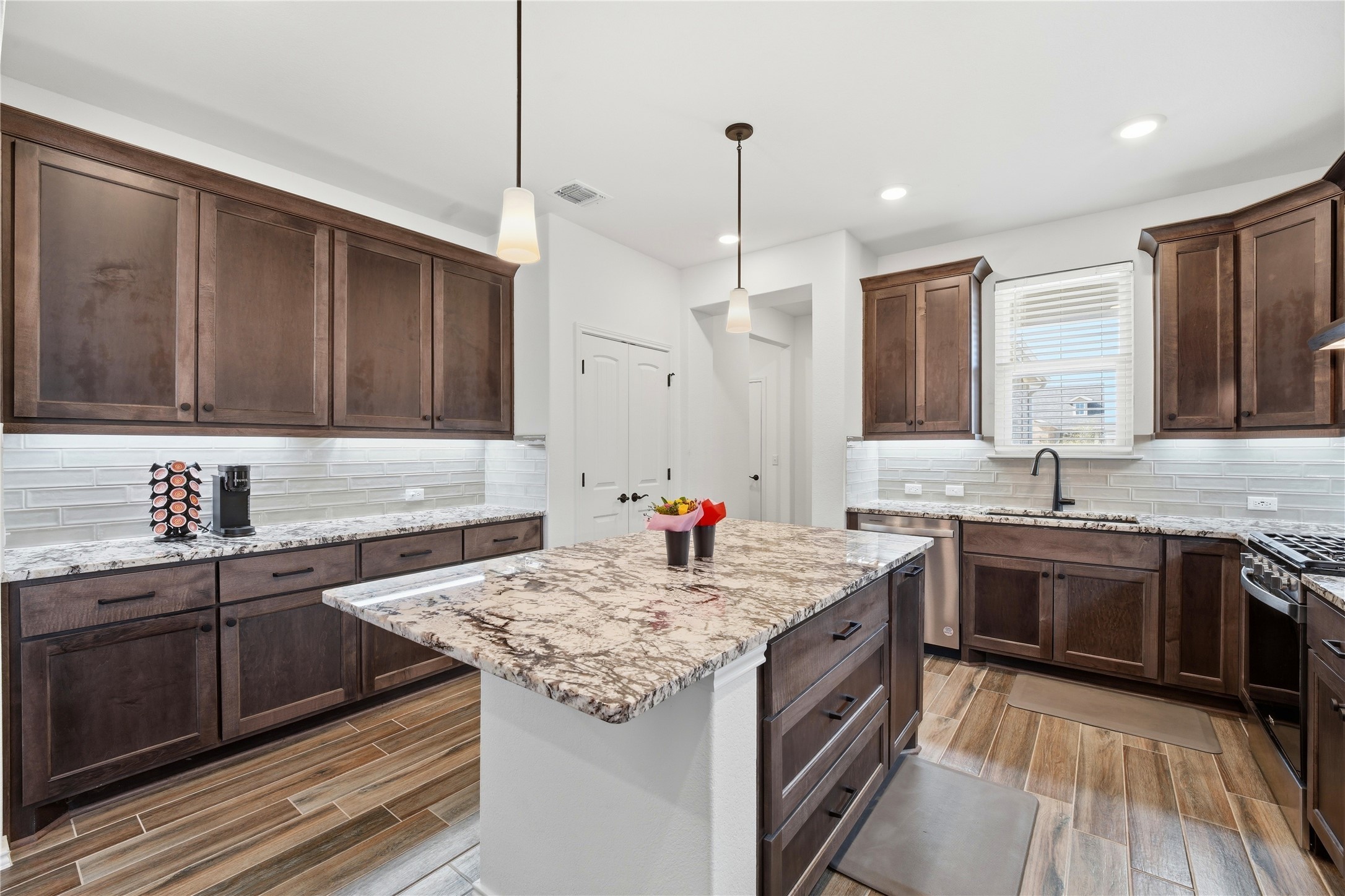 122 Clay Hl Street Georgetown, TX 78633 - Photo 7 of 31 Kitchen featuring light stone countertops, a kitchen island, hanging light fixtures, dark wood finish cabinetry, and wood finish floors