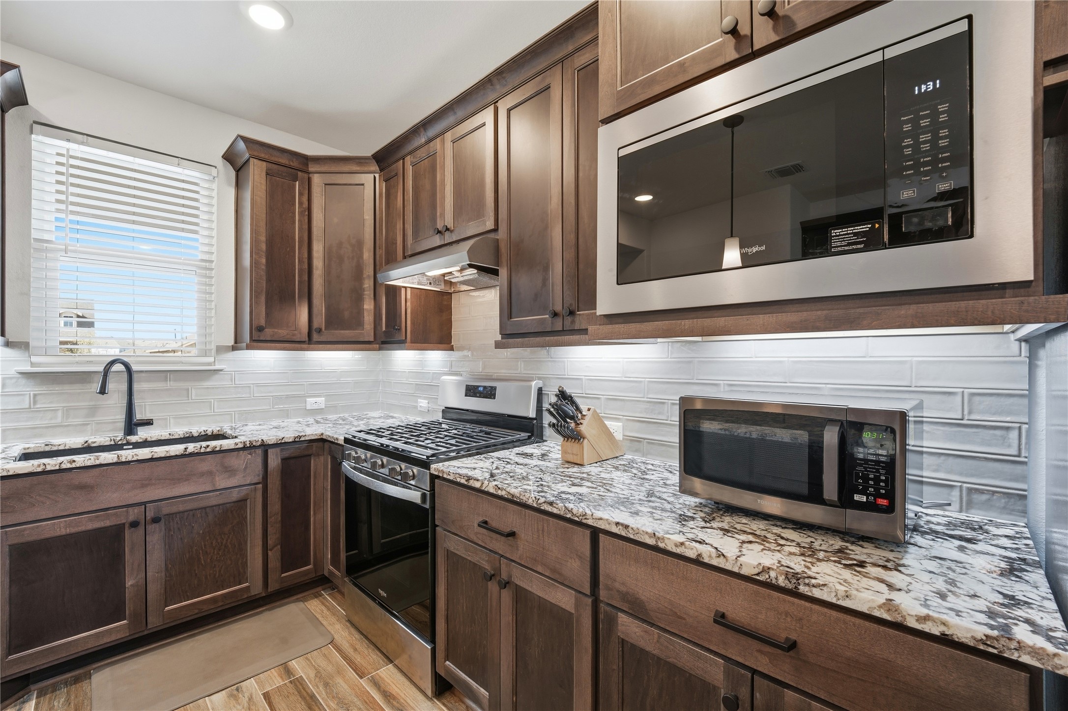122 Clay Hl Street Georgetown, TX 78633 - Photo 9 of 31 Kitchen featuring stainless steel appliances, dark wood finish cabinets, light stone countertops, tasteful backsplash, and light wood-style floors