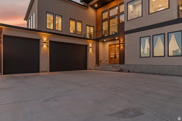 1445 Jacob Road Sandy, UT 84092 - Photo 64 of 65 Modern exterior with a large concrete driveway, two dark garage doors, and a wood-paneled entry featuring a double door