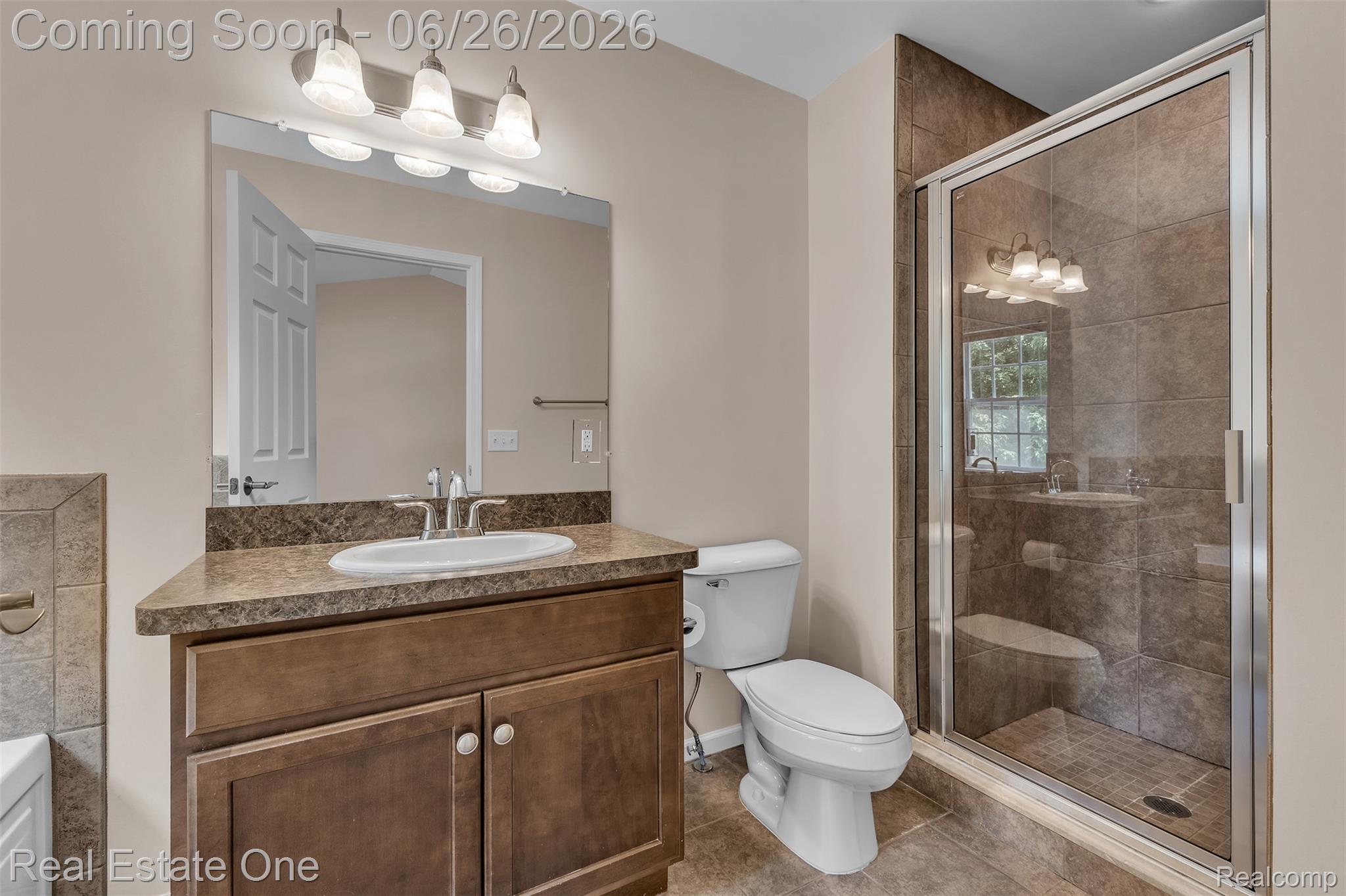 41590 Mitchell Road Novi, MI 48377 - Photo 32 of 45 Full bathroom featuring a glass-enclosed shower with tile surround, a single vanity with wood-finish cabinetry, a white oval sink, and a multi-bulb vanity light fixture