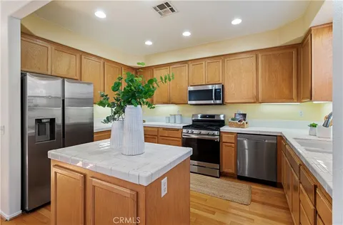 a kitchen with stainless steel appliances granite countertop a sink a stove a refrigerator a microwave with wooden cabinets and a window