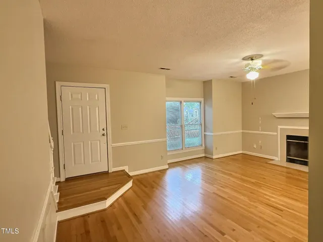 an empty room with wooden floor fireplace and windows