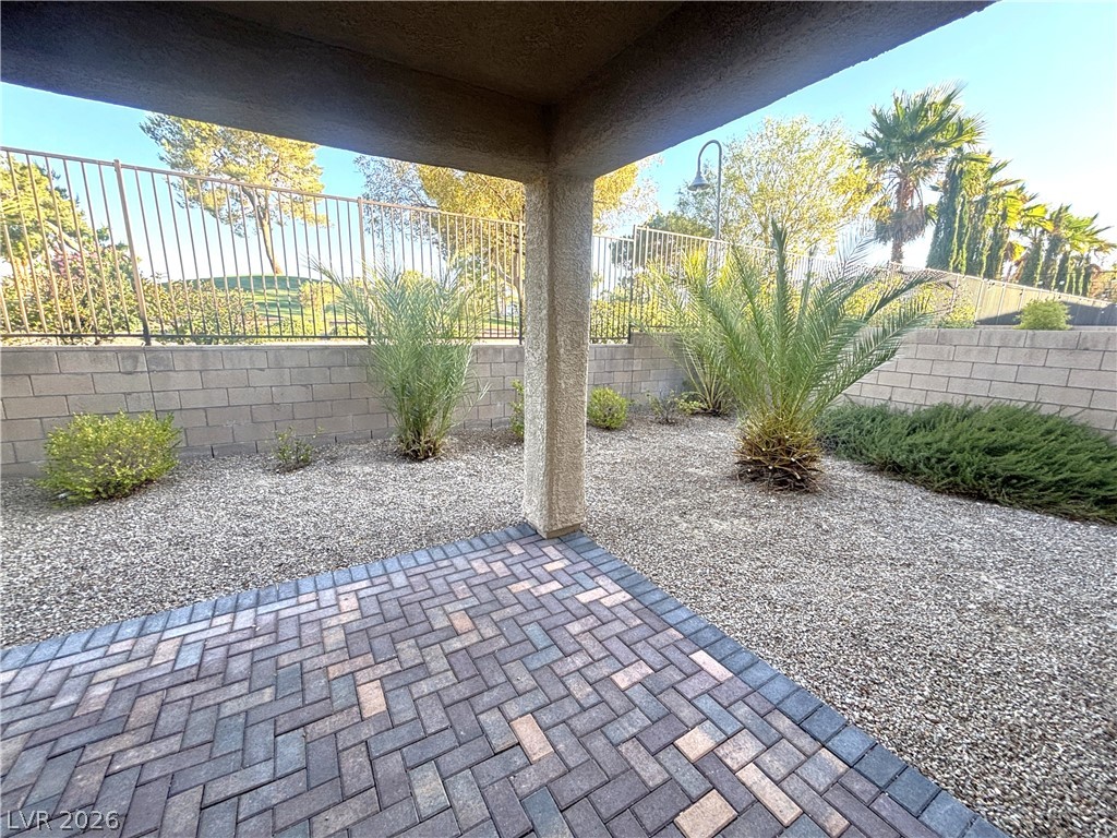 121 Elm Reed Avenue Las Vegas, NV 89113 - Photo 27 of 30 A private paved patio transitions to a gravel yard, enclosed by a block wall and ornamental fencing.