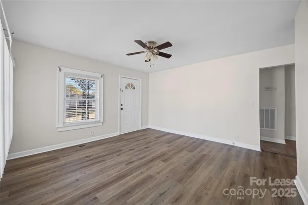 an empty room with wooden floor ceiling fan and windows