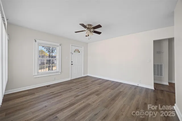 an empty room with wooden floor ceiling fan and windows