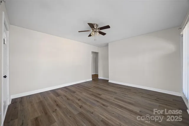 a view of an empty room with wooden floor and a ceiling fan