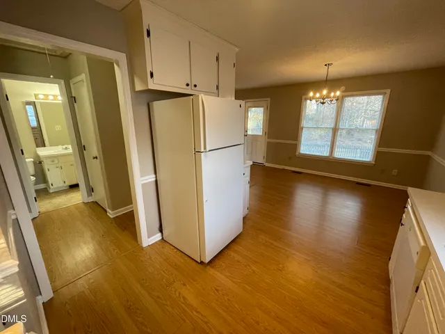 a view of a refrigerator in kitchen and an empty room with wooden floor