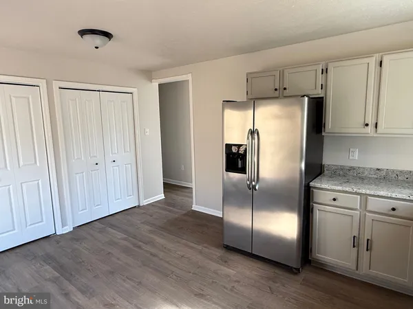 a kitchen with stainless steel appliances granite countertop a refrigerator a sink and white cabinets with wooden floors