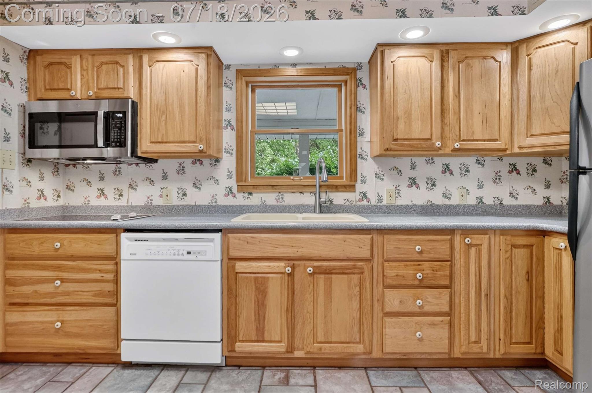 1437 East Cook Road Grand Blanc, MI 48439 - Photo 45 of 69 Kitchen featuring light wood cabinetry, a stainless steel microwave, a white dishwasher, a window over the sink, and recessed lighting