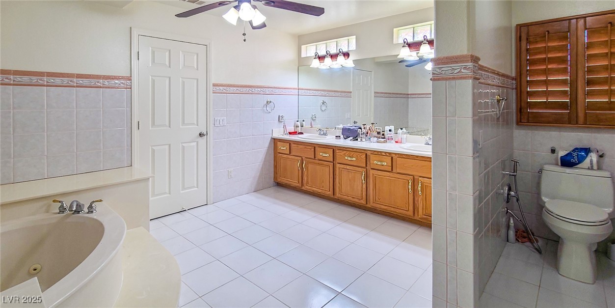 4100 Highland Castle Court Las Vegas, NV 89129 - Photo 24 of 49 Full bathroom with tile walls, double vanity, light tile patterned floors, a ceiling fan, and wainscoting