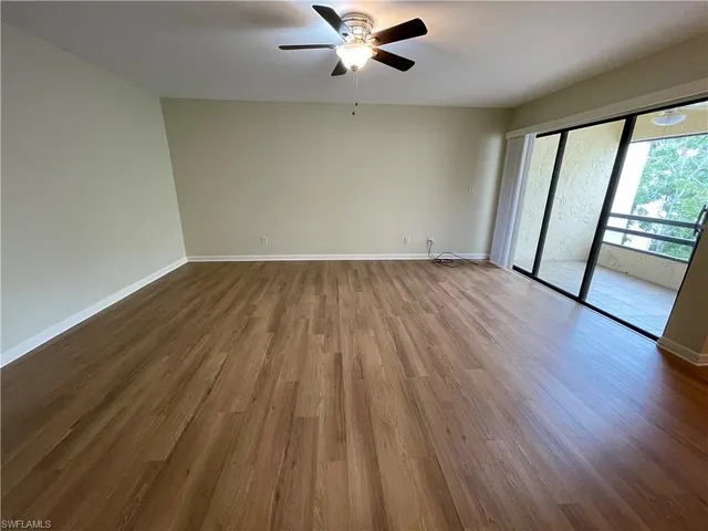 an empty room with wooden floor fan and window