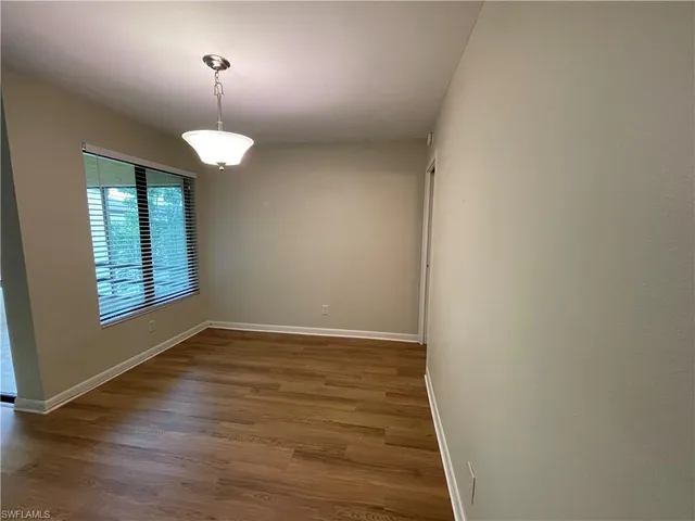 an empty room with wooden floor chandelier and windows