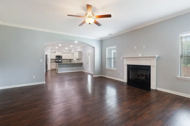 an empty room with wooden floor a ceiling fan a fireplace and windows