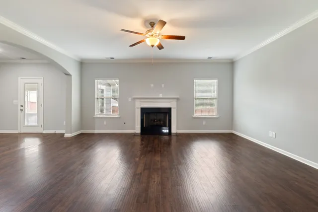 an empty room with wooden floor chandelier fan and windows