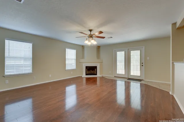 an empty room with wooden floor fireplace and windows