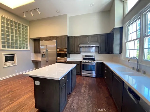 a kitchen with stainless steel appliances kitchen island granite countertop a refrigerator a sink dishwasher a stove with wooden cabinets and floor