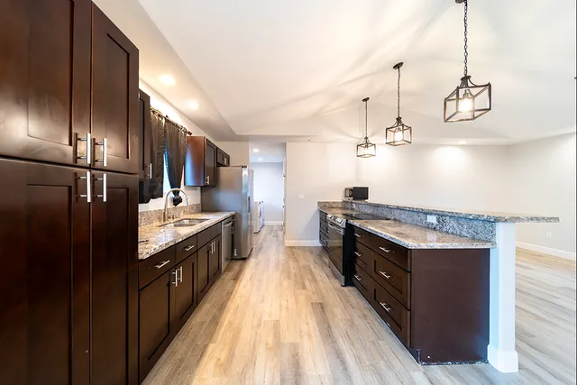 a large kitchen with stainless steel appliances granite countertop a stove a refrigerator and a sink with wooden floor