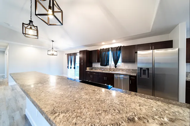 a kitchen with stainless steel appliances granite countertop a refrigerator a stove and a sink with wooden floor