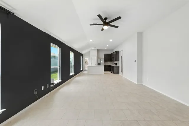 a view of an empty room and kitchen with chandelier ceiling fan