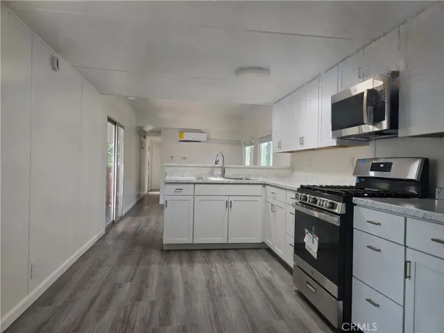 a kitchen with stainless steel appliances granite countertop a stove top oven a sink dishwasher and white cabinets with wooden floor