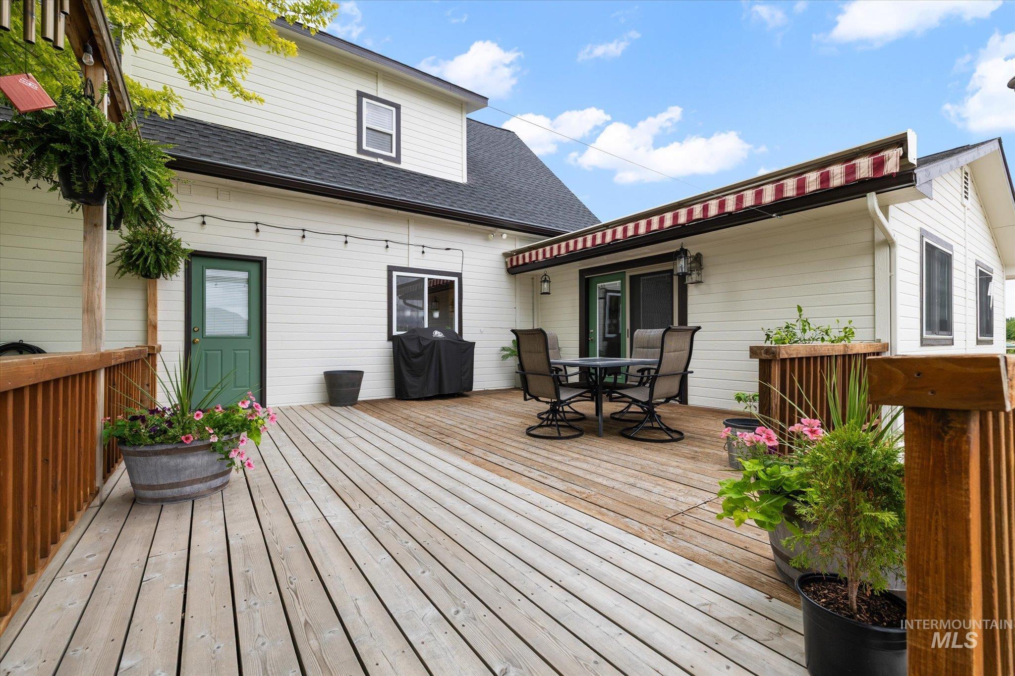 1140 Edgemont Road Emmett, ID 83617 - Photo 27 of 50 Expansive wood-finish decking featuring white horizontal siding, dark trim windows, a green entry door, and a striped retractable awning