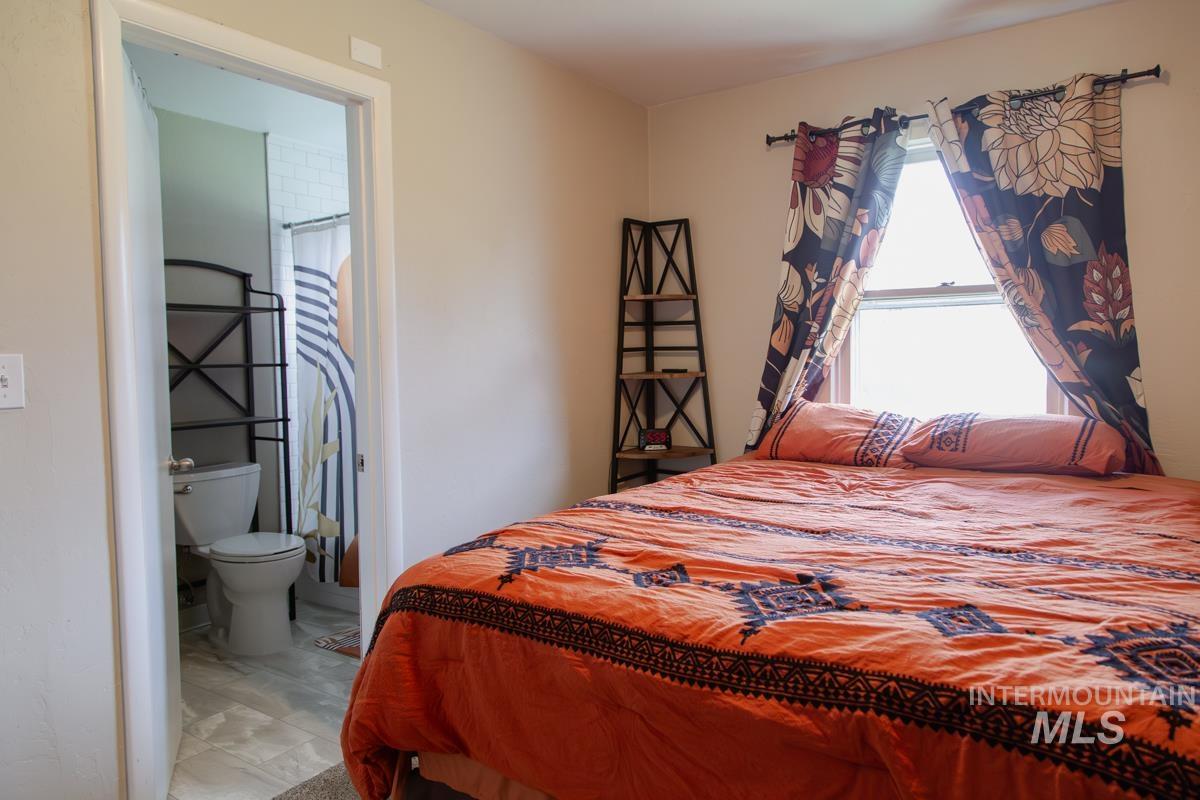 1404 Rochester Street Caldwell, ID 83605 - Photo 11 of 29 Bedroom featuring a window with a single-hung pane, neutral wall paint, and a doorway opening to a bathroom with a white toilet and patterned shower curtain
