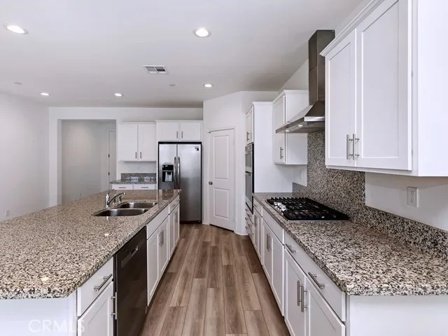 a kitchen with stainless steel appliances granite countertop a stove top oven a sink dishwasher a refrigerator and white cabinets with wooden floor