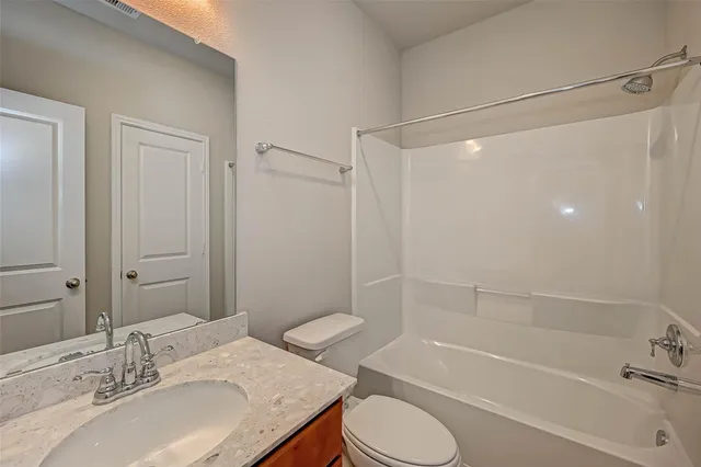 a bathroom with a granite countertop bathtub shower sink vanity and toilet