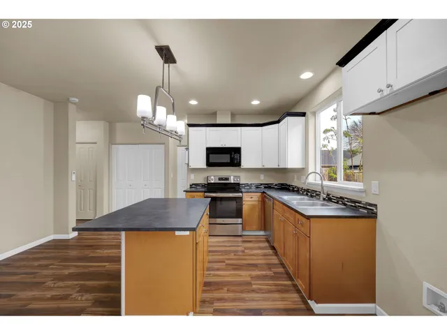 a kitchen with stainless steel appliances granite countertop a stove top oven a sink dishwasher and a refrigerator with wooden floor