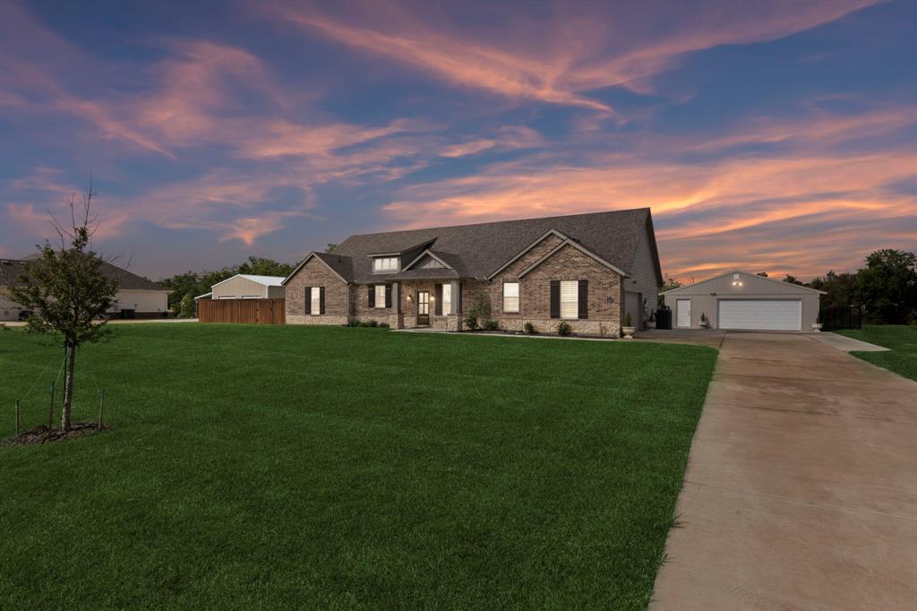 View of front of house with a front yard, concrete driveway, an outbuilding, and stone siding