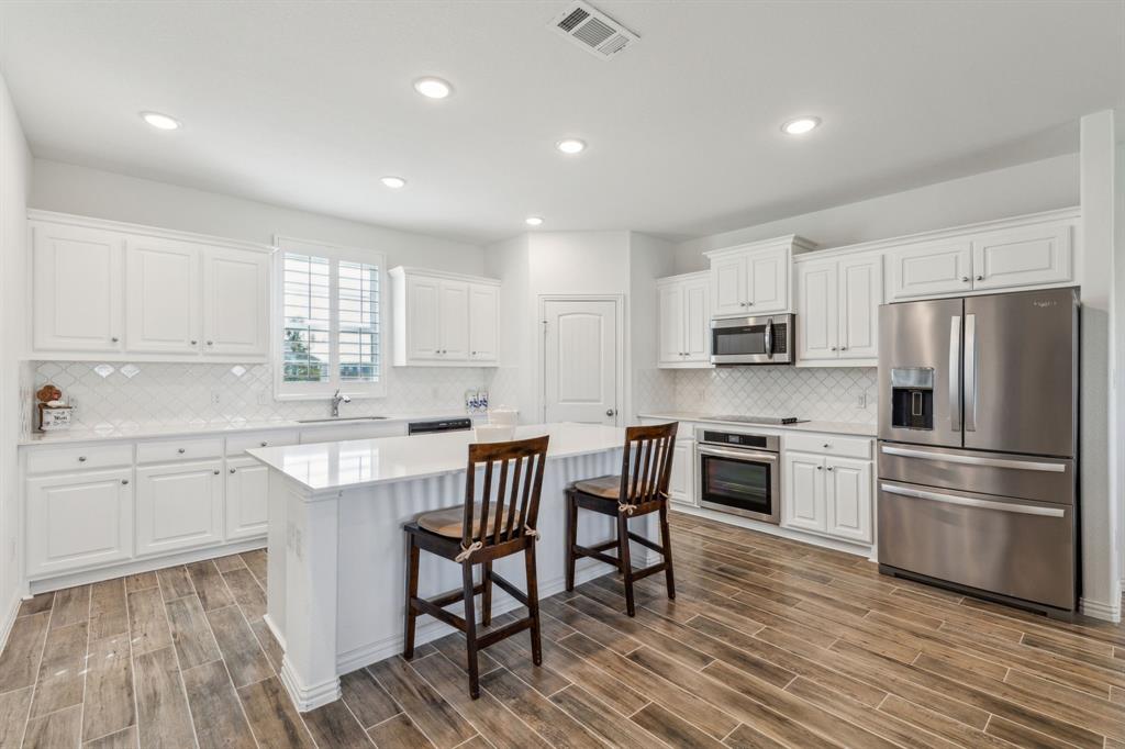 2410 Black Jack Oak Road Terrell, TX 75161 - Photo 11 of 31 Kitchen featuring appliances with stainless steel finishes, a sink, white cabinets, a breakfast bar area, and wood finished floors