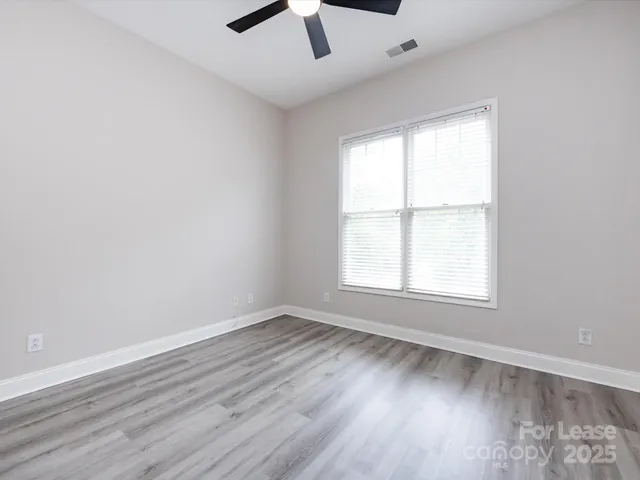 an empty room with wooden floor fan and windows