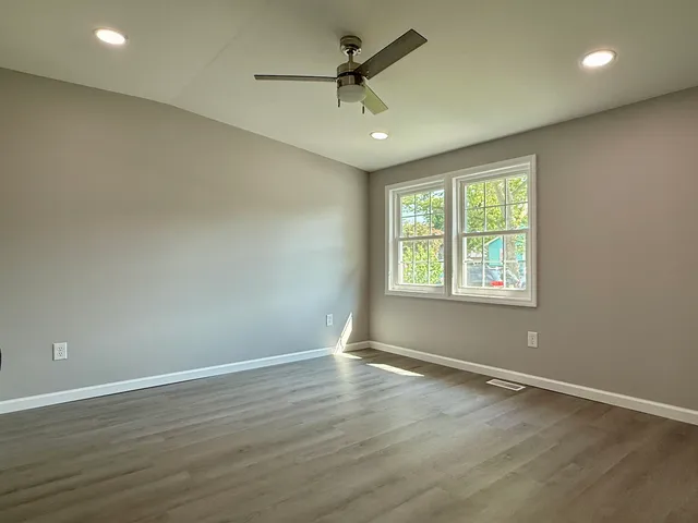 an empty room with wooden floor chandelier fan and windows