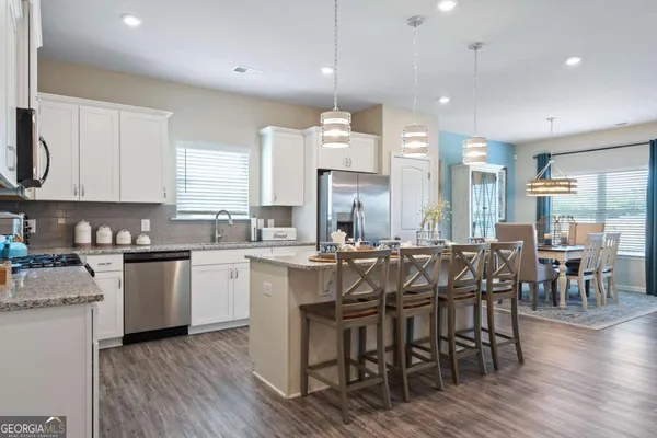 a large kitchen with cabinets wooden floor white stainless steel appliances and chairs