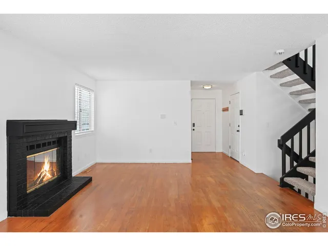 a view of an empty room with wooden floor fireplace and a window