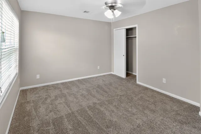 an empty room with chandelier fan and windows