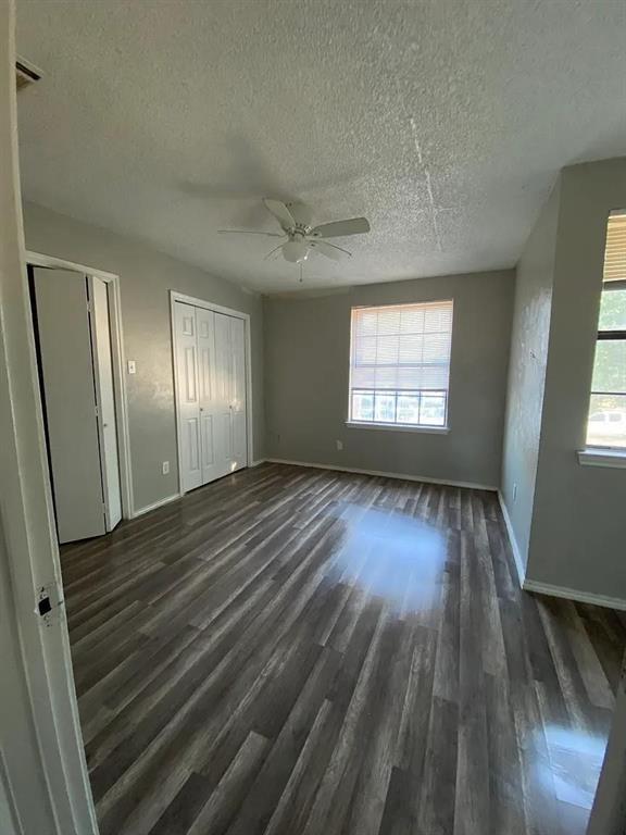 Unfurnished bedroom featuring dark wood finished floors, ceiling fan, multiple windows, and a textured ceiling