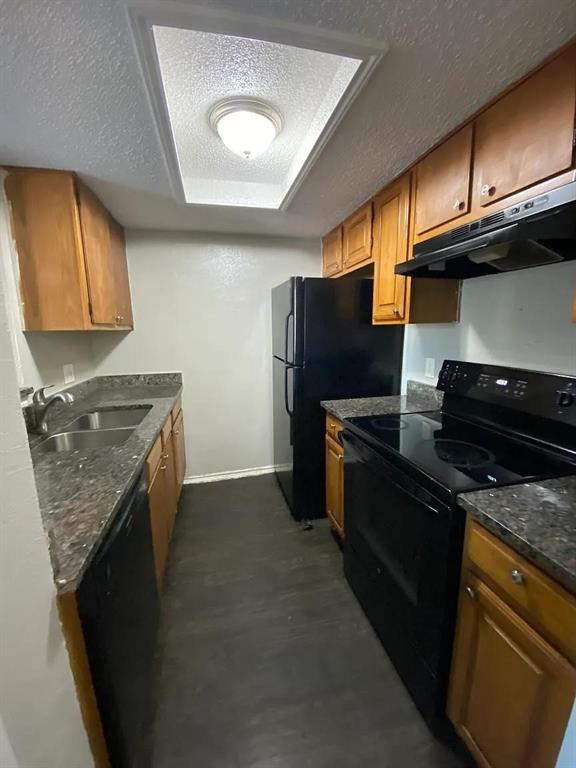 8005 Rothington Road, Unit 51 Dallas, TX 75227 - Photo 3 of 9 Kitchen with a textured ceiling, black appliances, dark stone countertops, under cabinet range hood, and brown cabinets