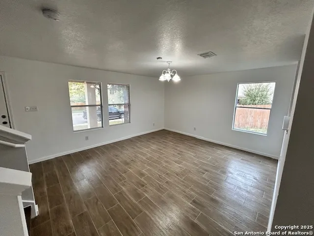 an empty room with wooden floor chandelier and windows