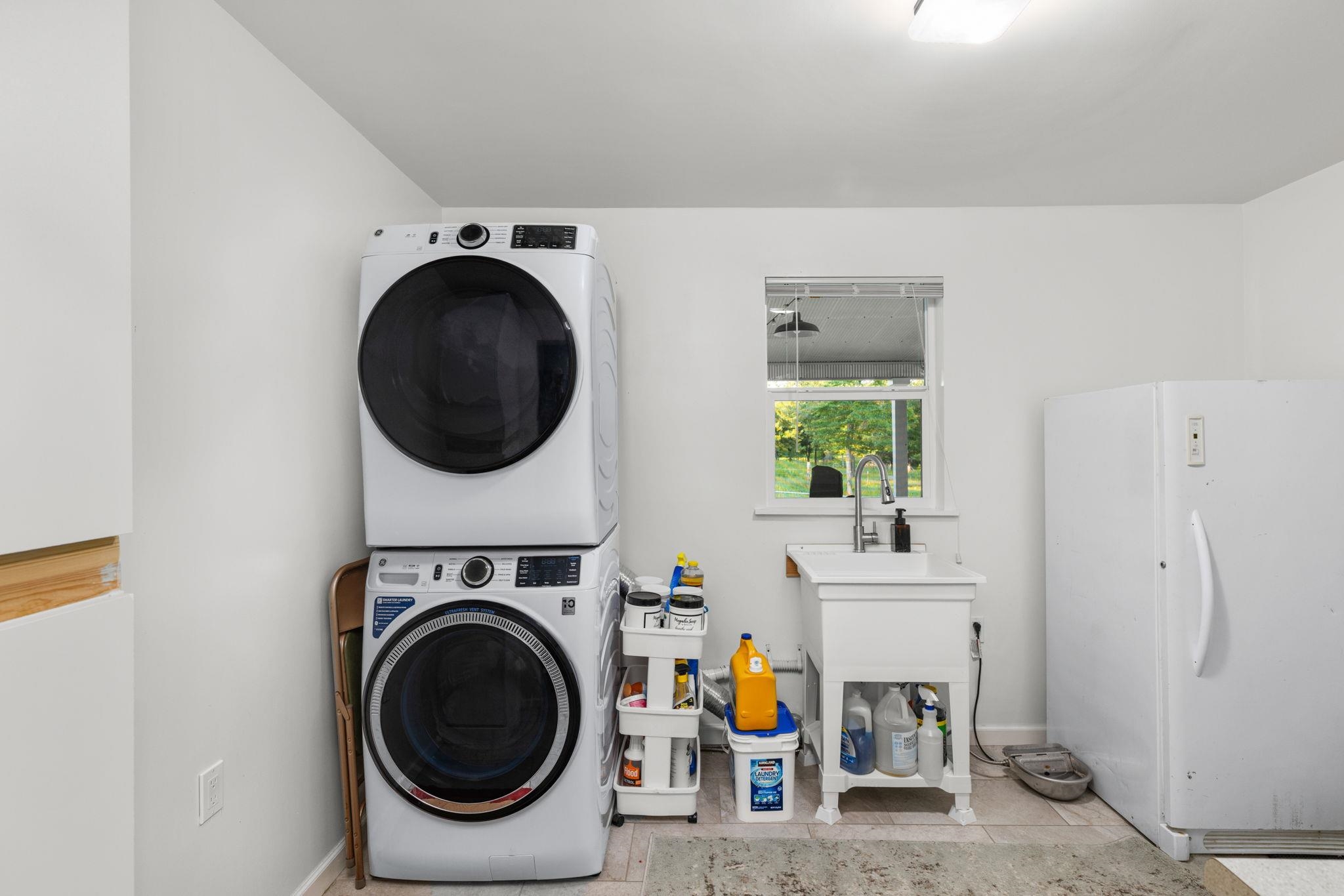 66 County Road 511 Corinth, MS 38834 - Photo 23 of 40 Bright utility space featuring a stacked washer and dryer, a window with natural light, a white utility sink with a chrome faucet, and a large white freestanding refrigerator