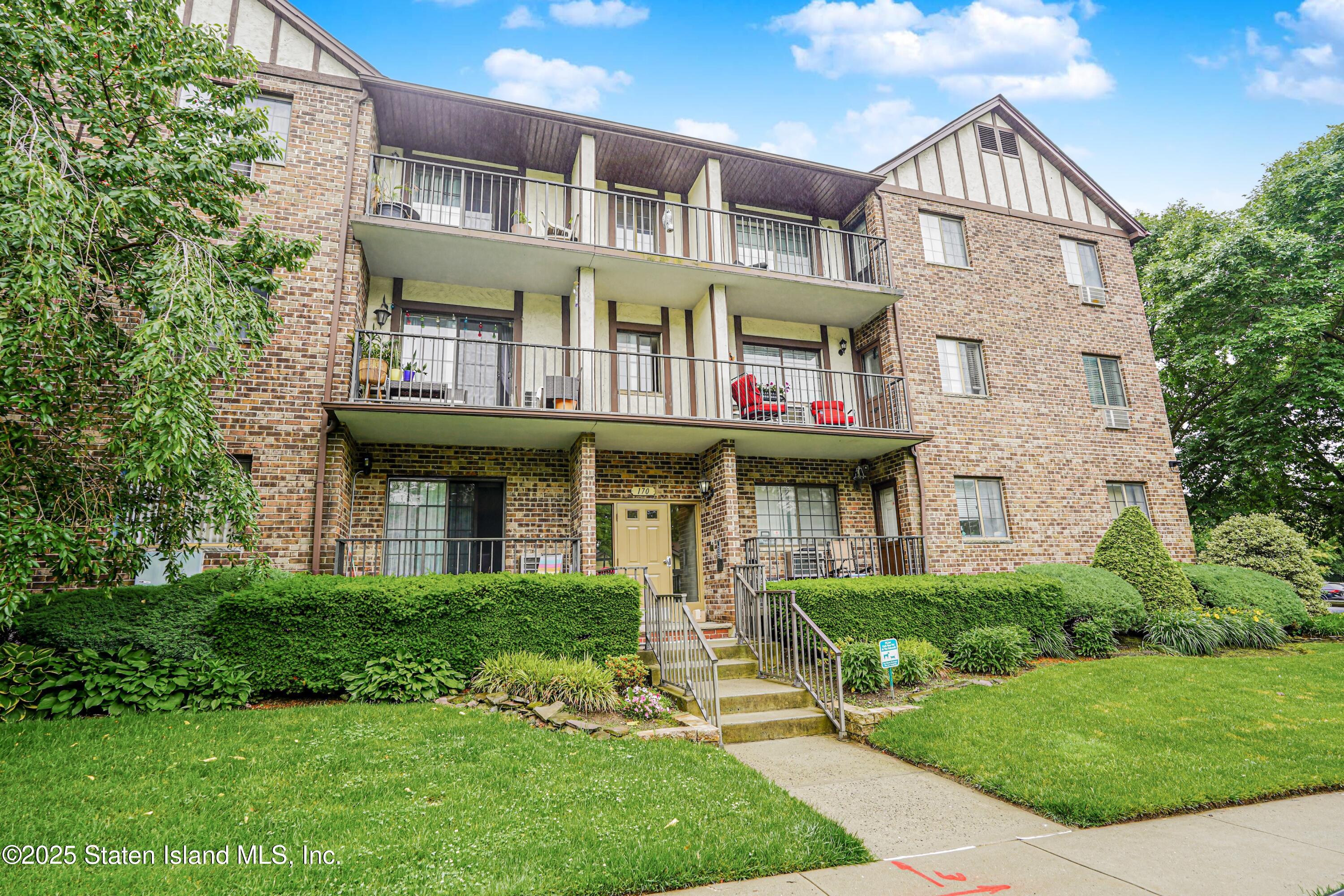 a view of a brick building with many windows and a yard with plants and large trees