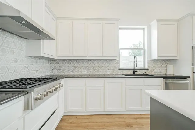 a kitchen with granite countertop a stove a sink and white cabinets with wooden floor next to windows