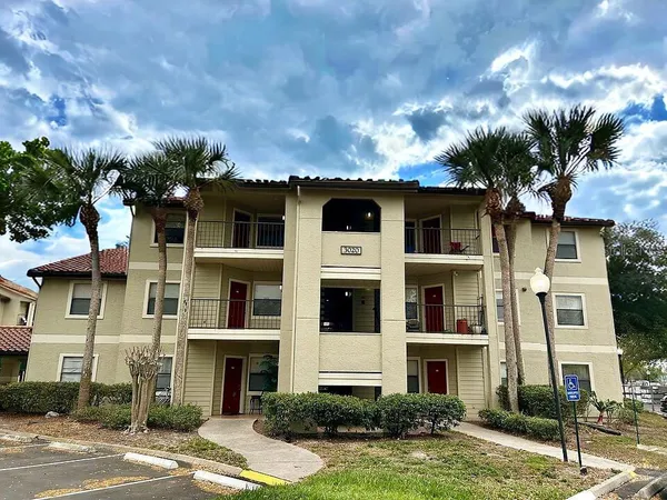 a front view of a multi story residential apartment building with yard and parking
