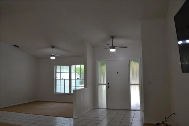 an empty room with chandelier fan and windows