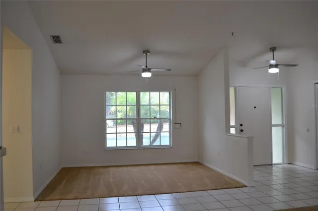 an empty room with chandelier fan and windows