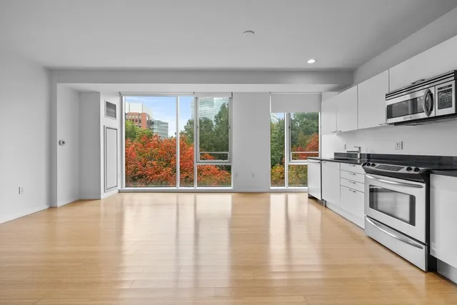 a large white kitchen with stainless steel appliances granite countertop a stove a sink and a large window
