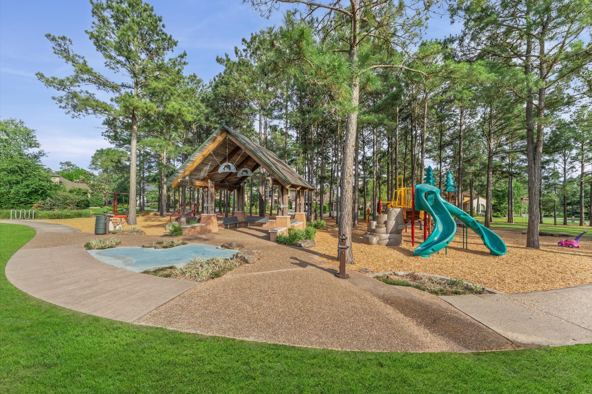 70 Valera Ridge Drive Spring, TX 77389 - Photo 37 of 37 This photo shows a charming park area with a playground featuring slides, climbing structures, and a covered pavilion. It's surrounded by tall trees and well-maintained paths, ideal for families and outdoor activities.