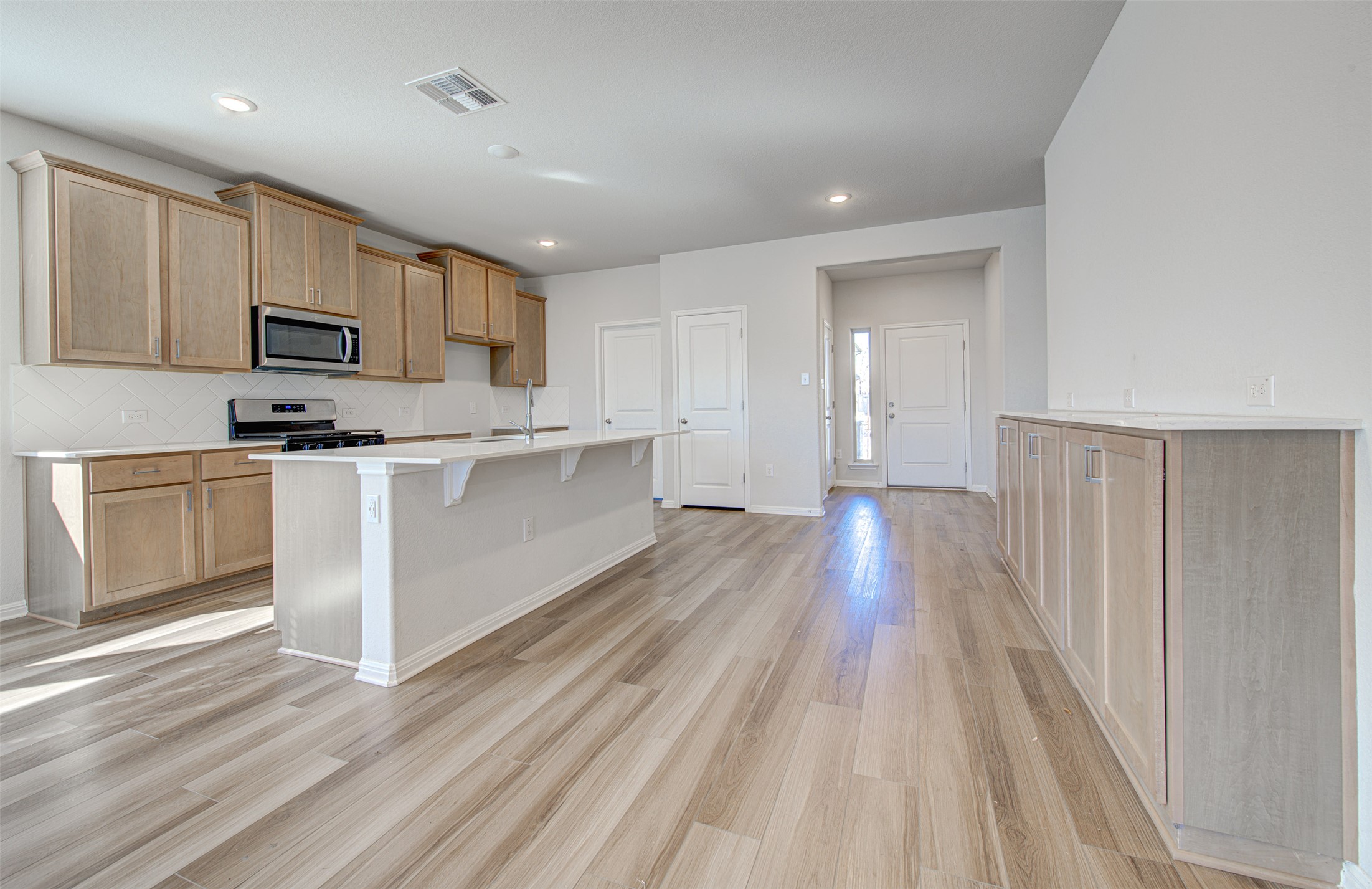 13129 Ditka Drive Manchaca, TX 78652 - Photo 4 of 32 Kitchen featuring a kitchen breakfast bar, stainless steel appliances, light wood-style flooring, decorative backsplash, and a center island with sink
