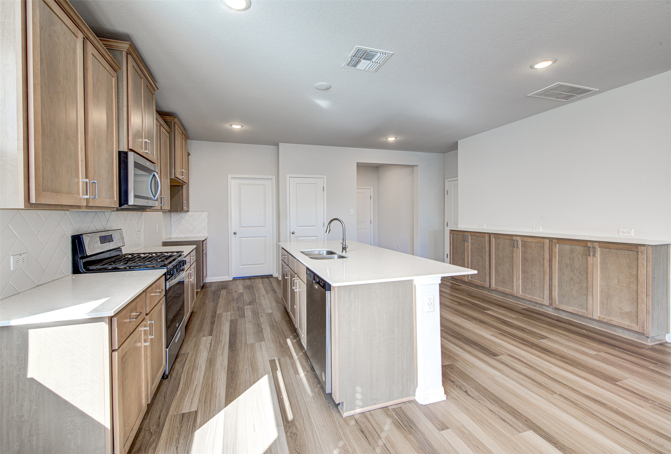 13129 Ditka Drive Manchaca, TX 78652 - Photo 5 of 32 Kitchen with stainless steel appliances, backsplash, light wood finished floors, a center island with sink, and light stone counters