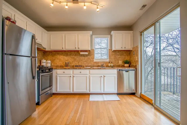 a kitchen with granite countertop a refrigerator oven a sink and white cabinets